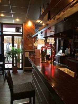 A bar area with a counter, stools, and a potted plant. - Hotel du Commerce (Semur-en-Auxois)