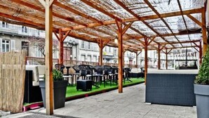Un café en plein air doté de pergolas en bois, de mobilier d’extérieur noir et offrant une vue sur un restaurant situé à l’arrière-plan.