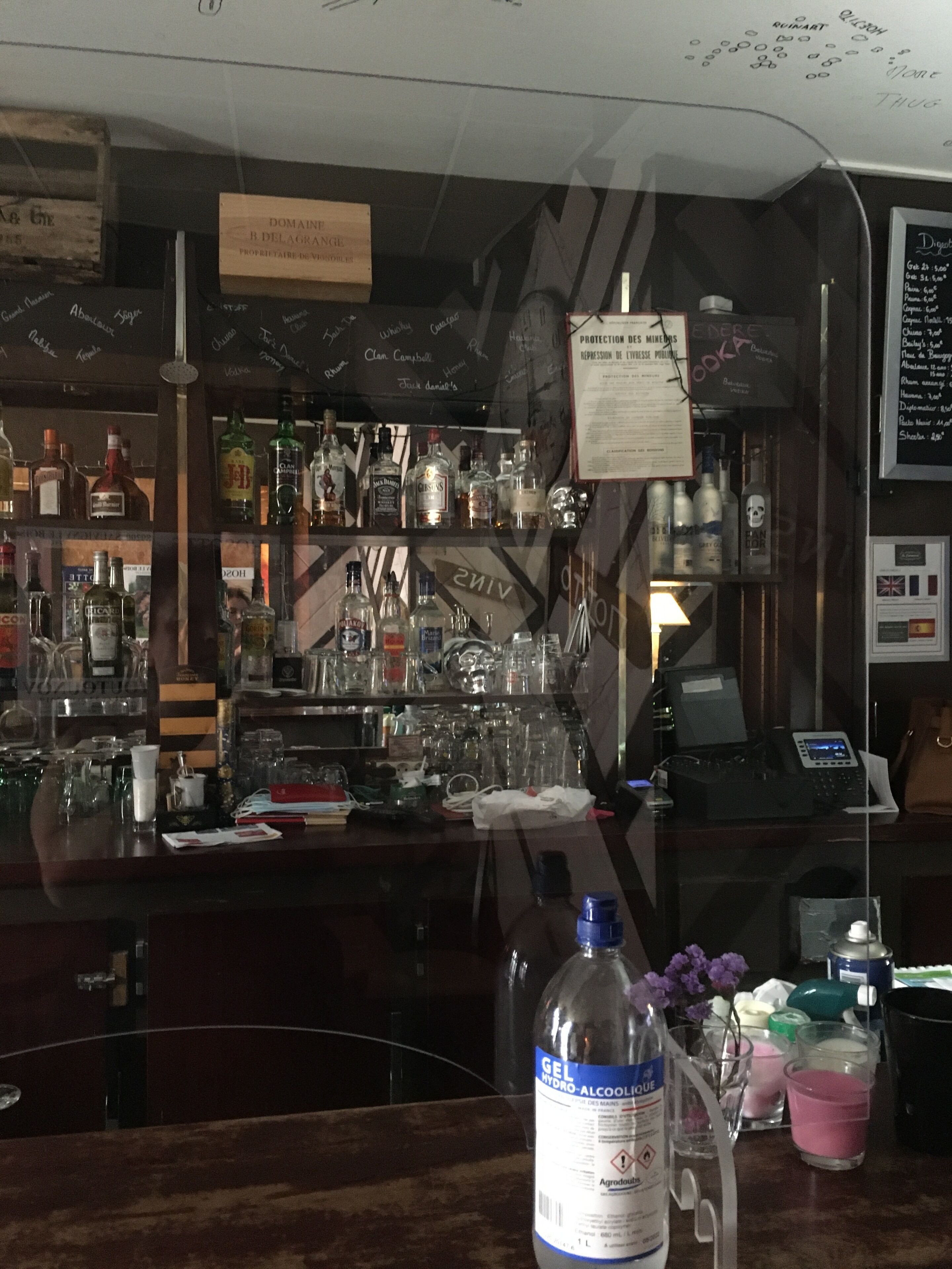 Una zona de bar con estantes llenos de botellas de licores, una pizarra con la carta y un ordenador portátil sobre la barra.