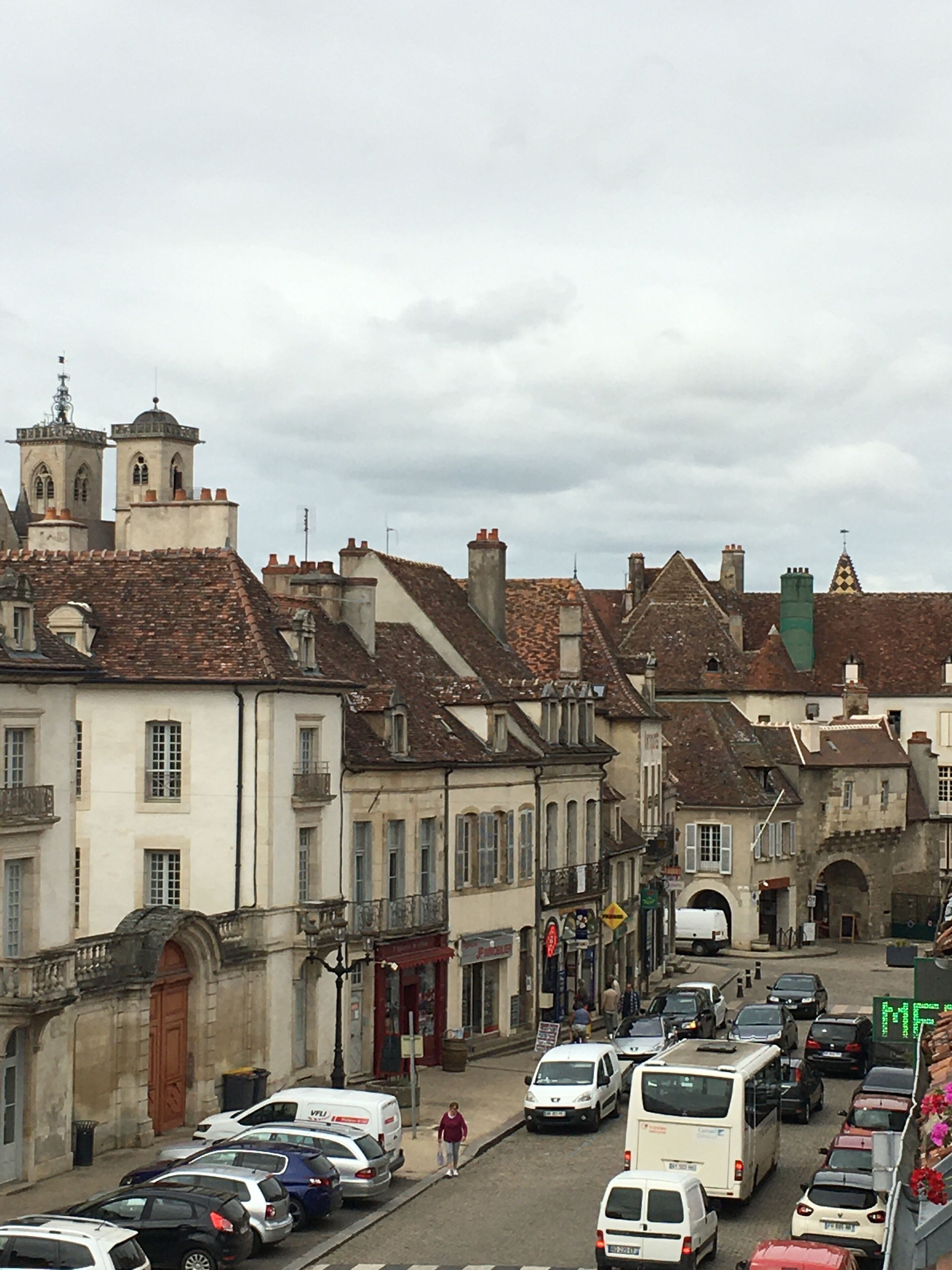 A street view with historic buildings, parked cars, and a pedestrian.
