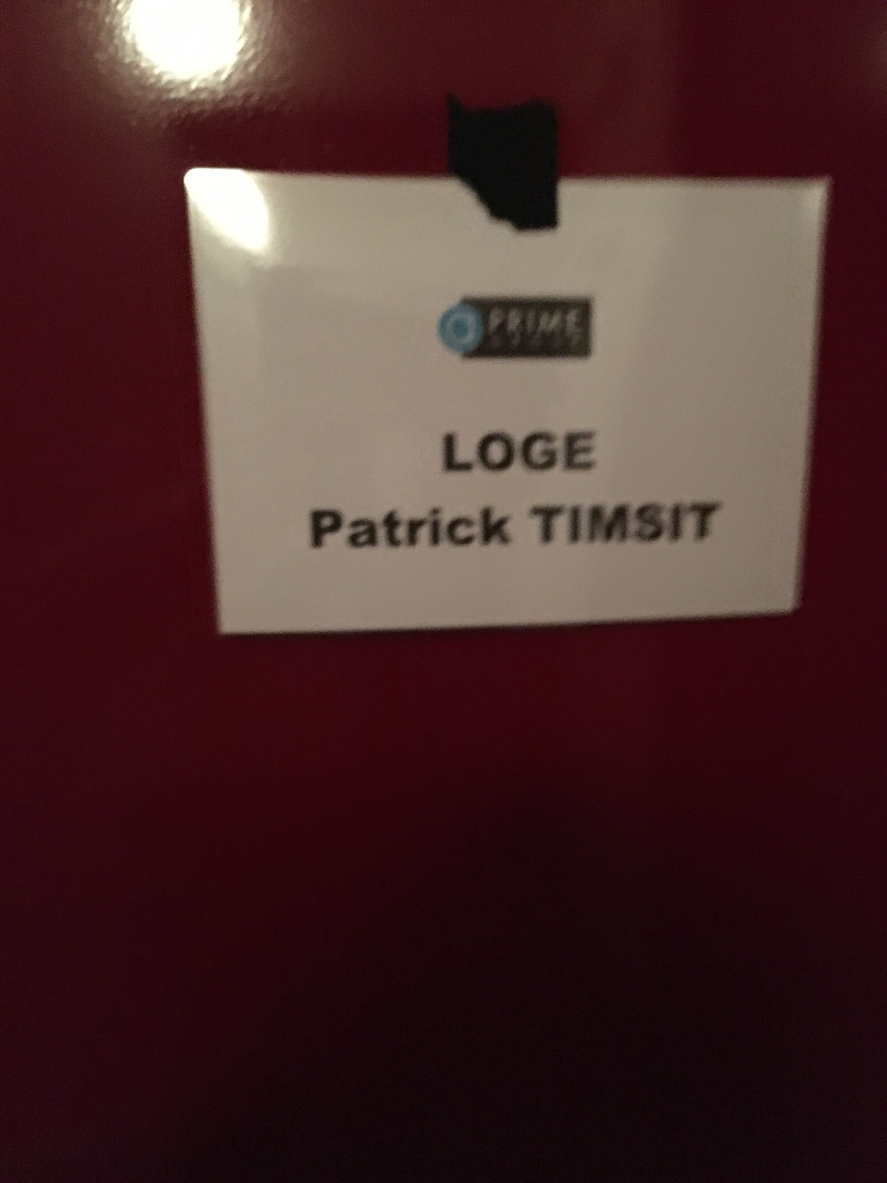 A sign with the name "LOGE Patrick TIMSIT" on a red wall.