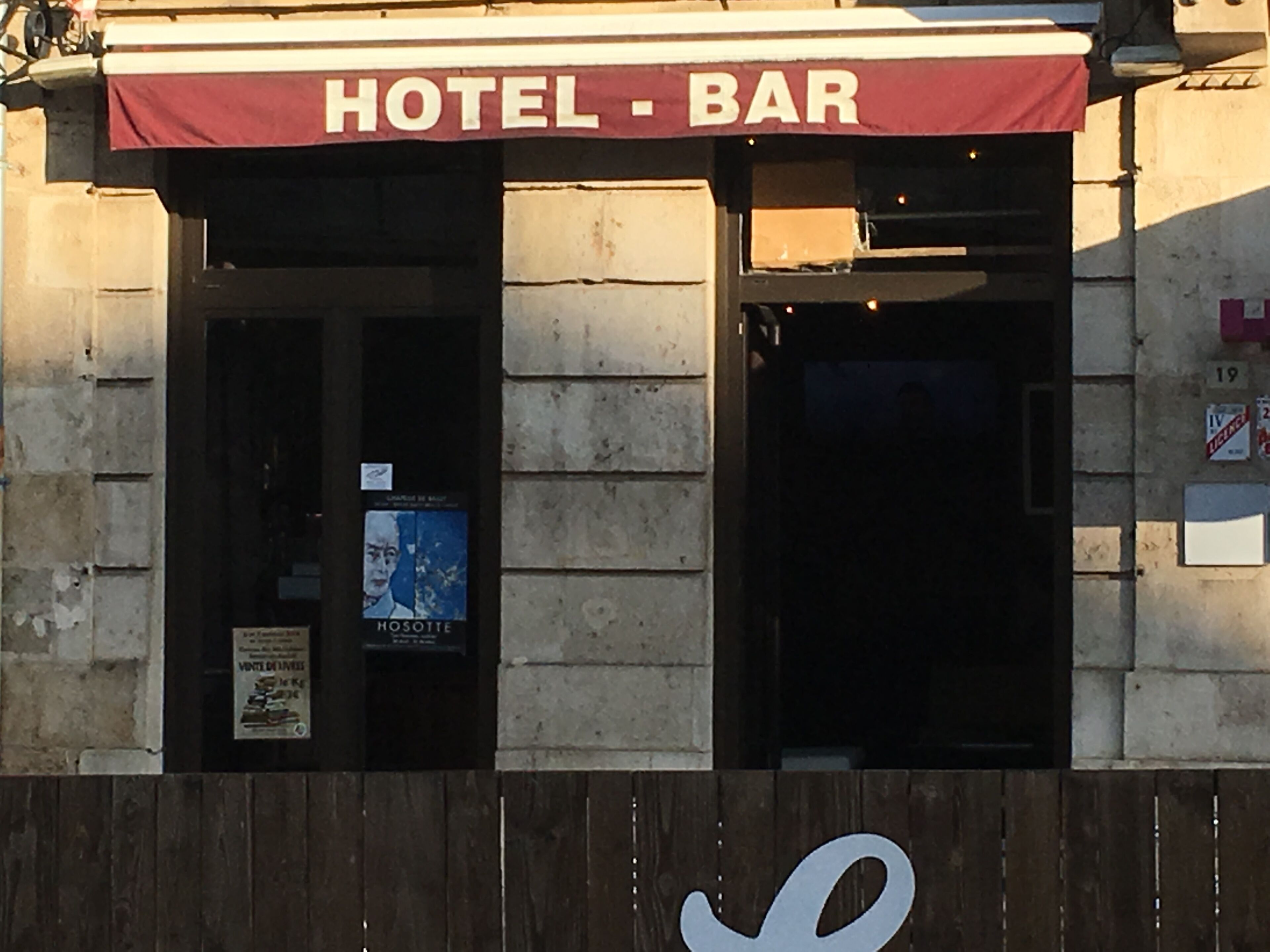 Un bar de hotel con un toldo rojo y una cerca de madera al frente.