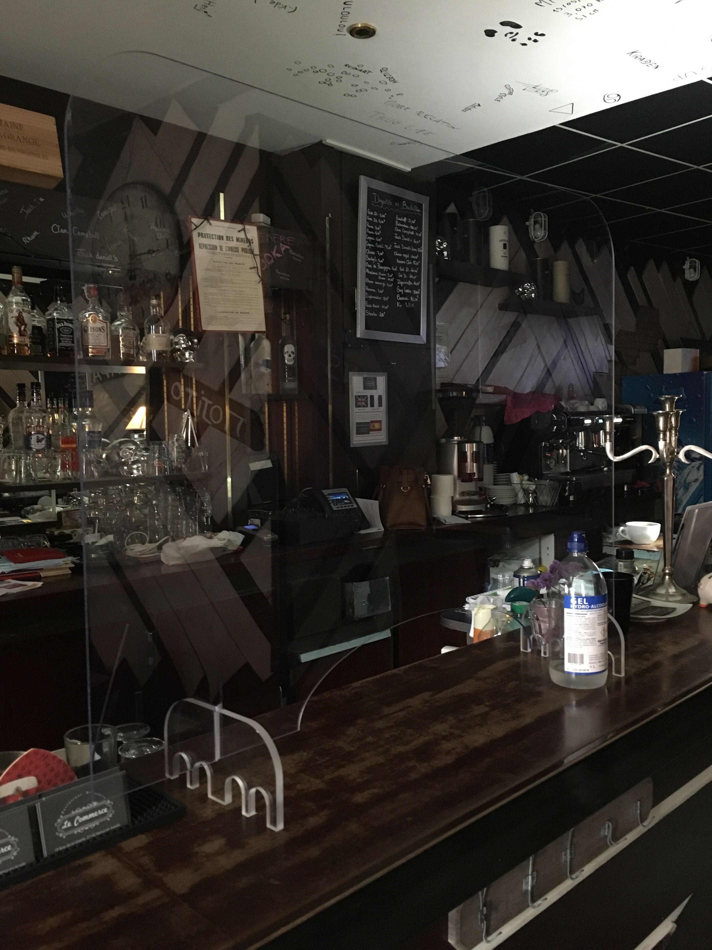 Un espace bar avec un comptoir en bois, des étagères remplies de bouteilles, un tableau affichant le menu et une horloge.