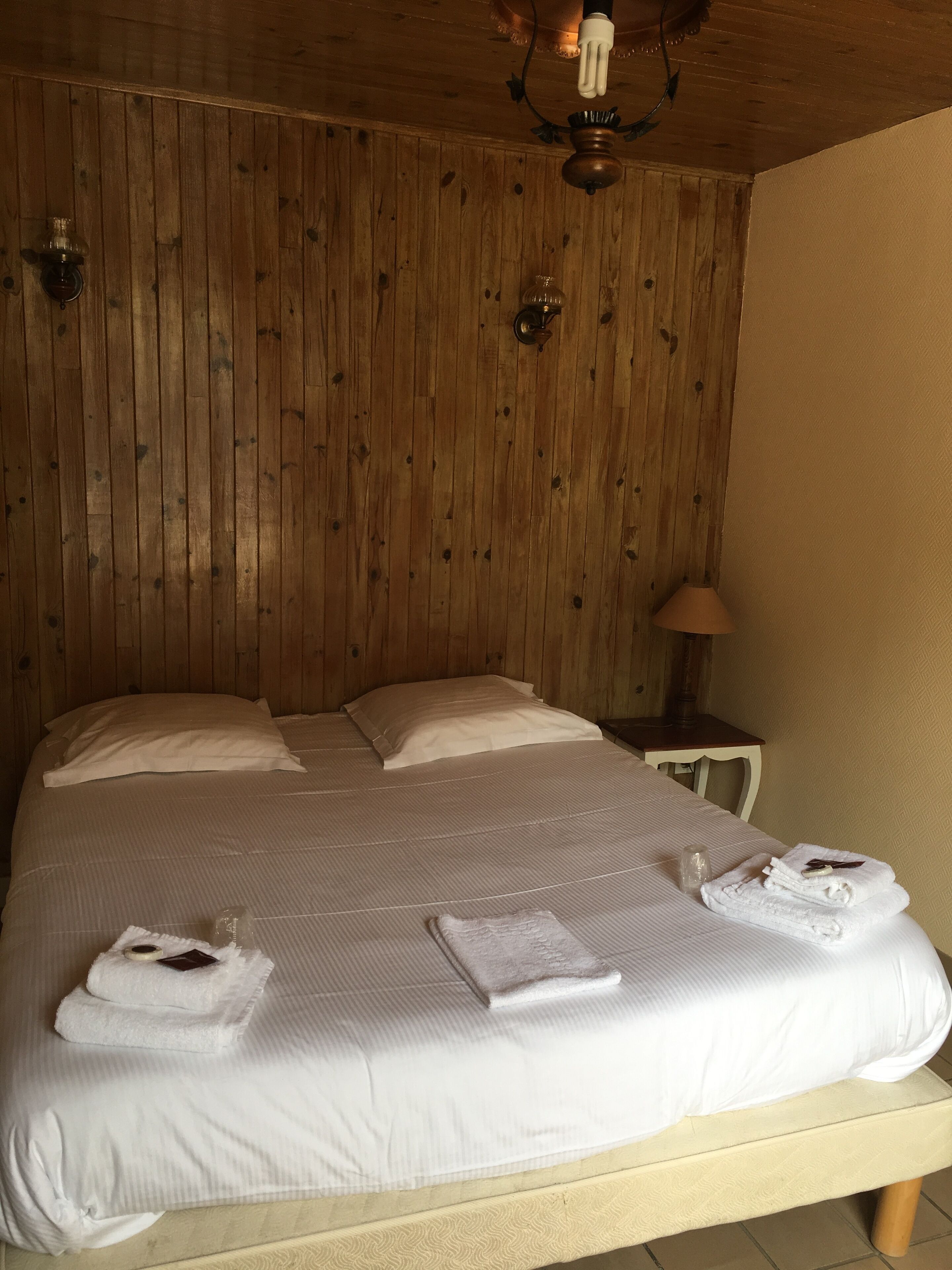 Un grand lit avec une tête de lit en bois, du linge de lit blanc et une table de chevet avec une lampe.