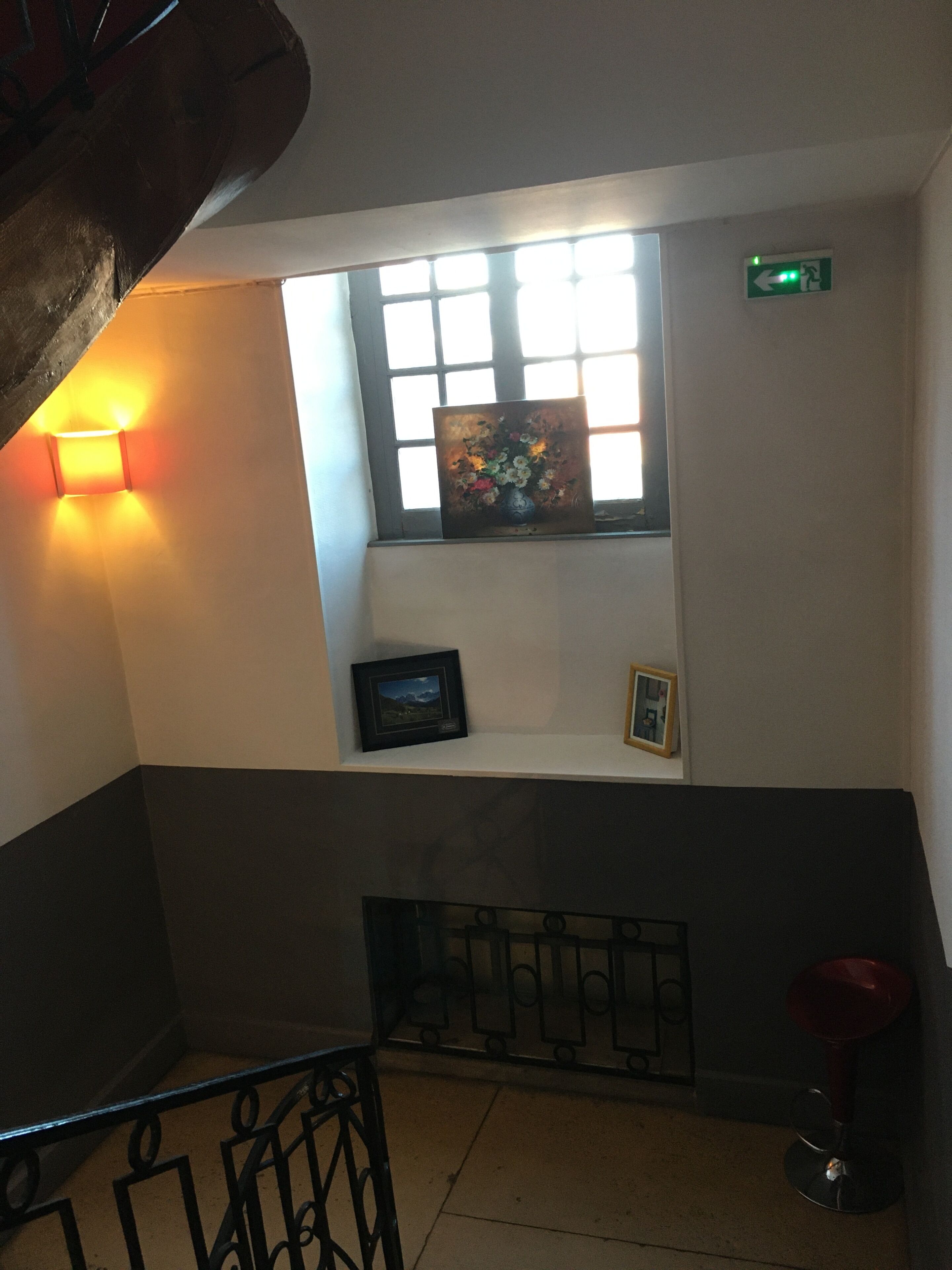 Un escalier avec une rampe, une fenêtre ornée d’un tableau et un luminaire fixé au mur.