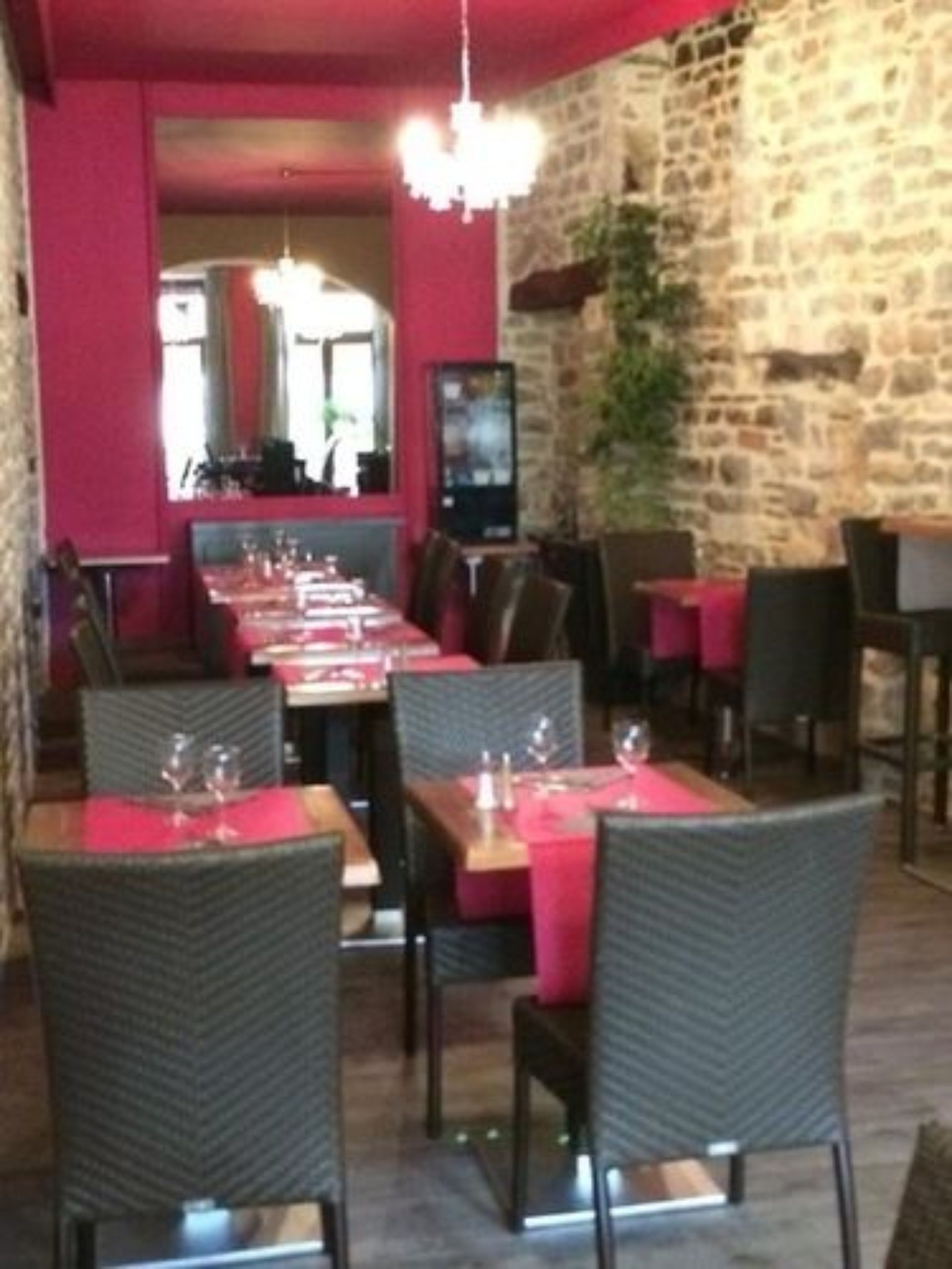 Un restaurant avec un mur en pierre, des murs rouges et une longue table à manger entourée de chaises.