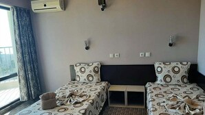 Ein Hotelzimmer mit zwei Betten, einem Fenster mit Vorhängen, einer Klimaanlage und einem kleinen Tisch.