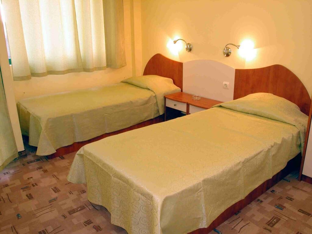 A room with two single beds, a wooden headboard, a nightstand, and a window with curtains.