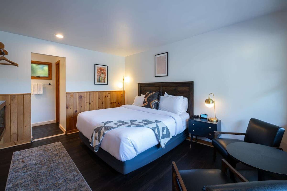 Een slaapkamer met een groot bed, een nachtkastje met een lamp, een stoel en een klein tafeltje.