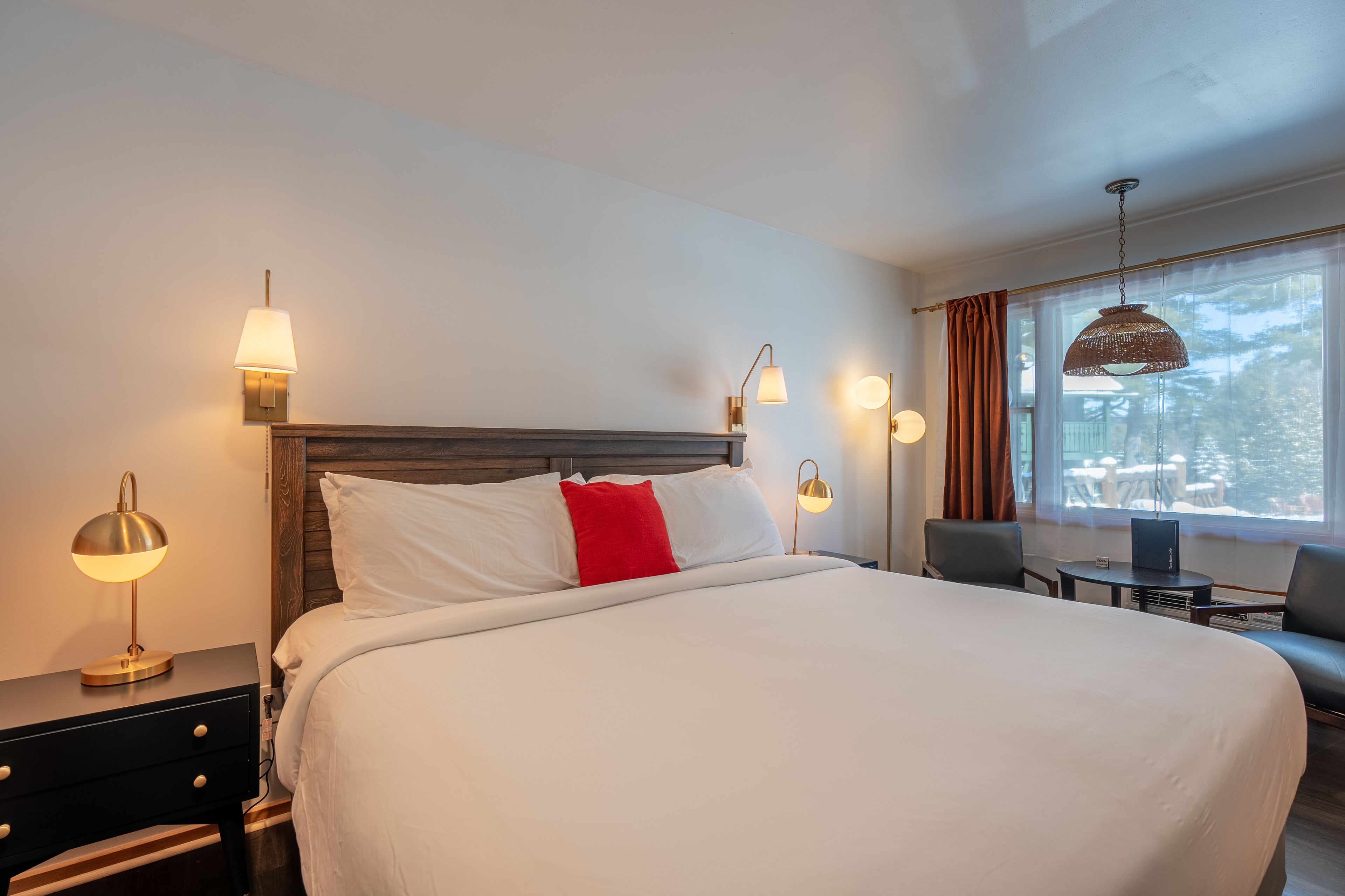 A hotel room with a large bed, bedside tables, a desk, and a window with curtains.