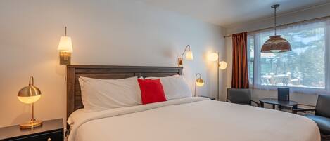 A hotel room with a large bed, bedside tables, a desk, and a window with curtains.
