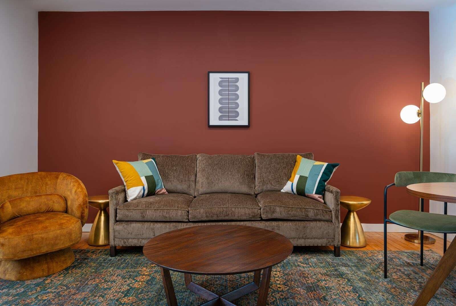 A modern living room with a brown sofa, a round wooden coffee table, a vintage armchair, and a small round table with a green chair.