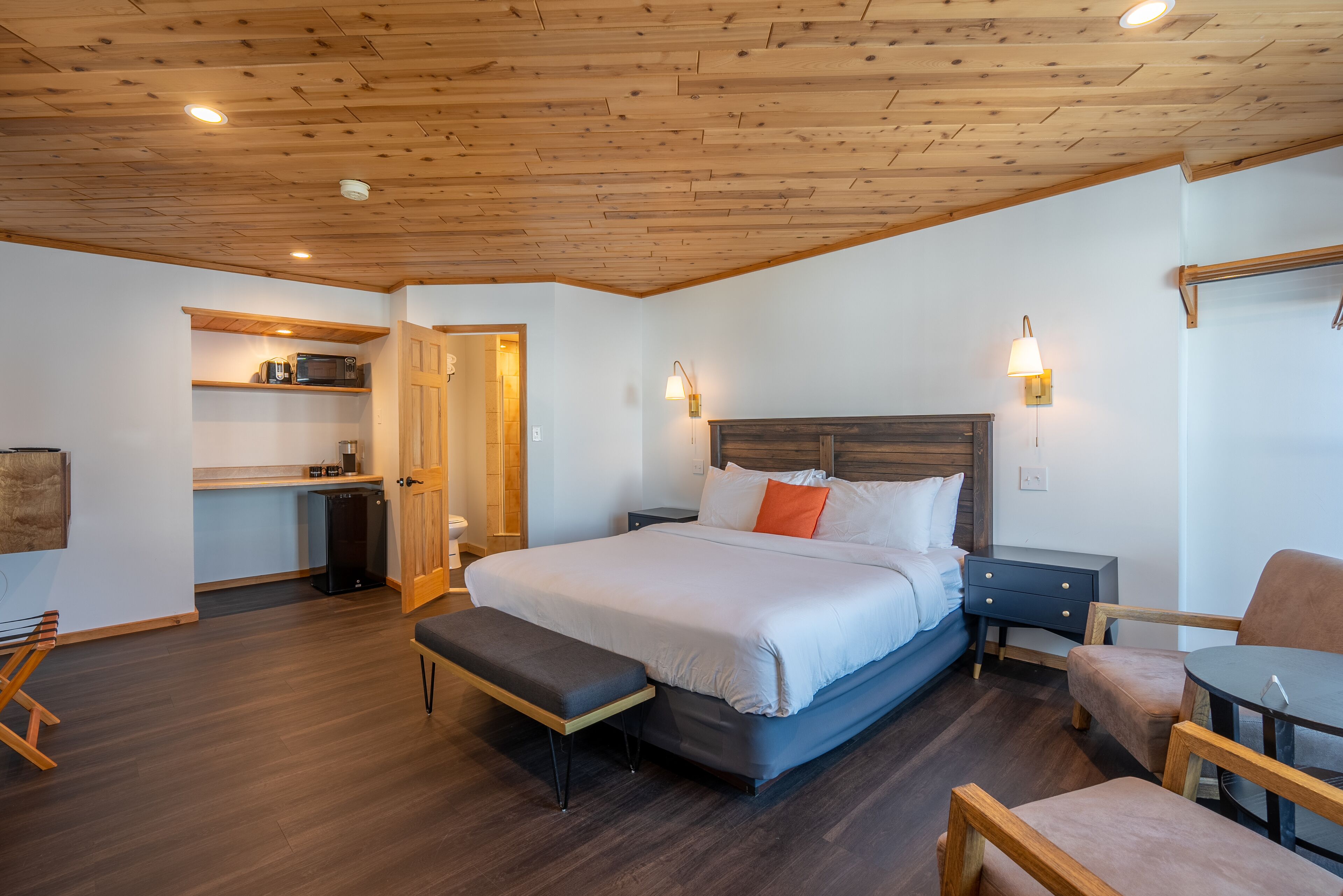 Een slaapkamer met een bed, een bankje, een nachtkastje en een klein bureau met een stoel.