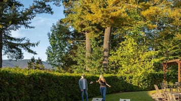 A grassy outdoor area with two shuffleboard tables and a pergola with seating.