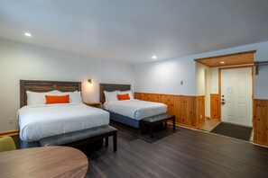 Une chambre d’hôtel avec deux lits, un banc, une table et une porte.