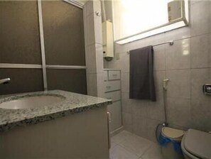 A bathroom with a granite countertop sink, a toilet, and a shower.