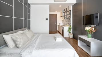 A modern hotel room with a large bed, a TV, and a kitchenette in the background.