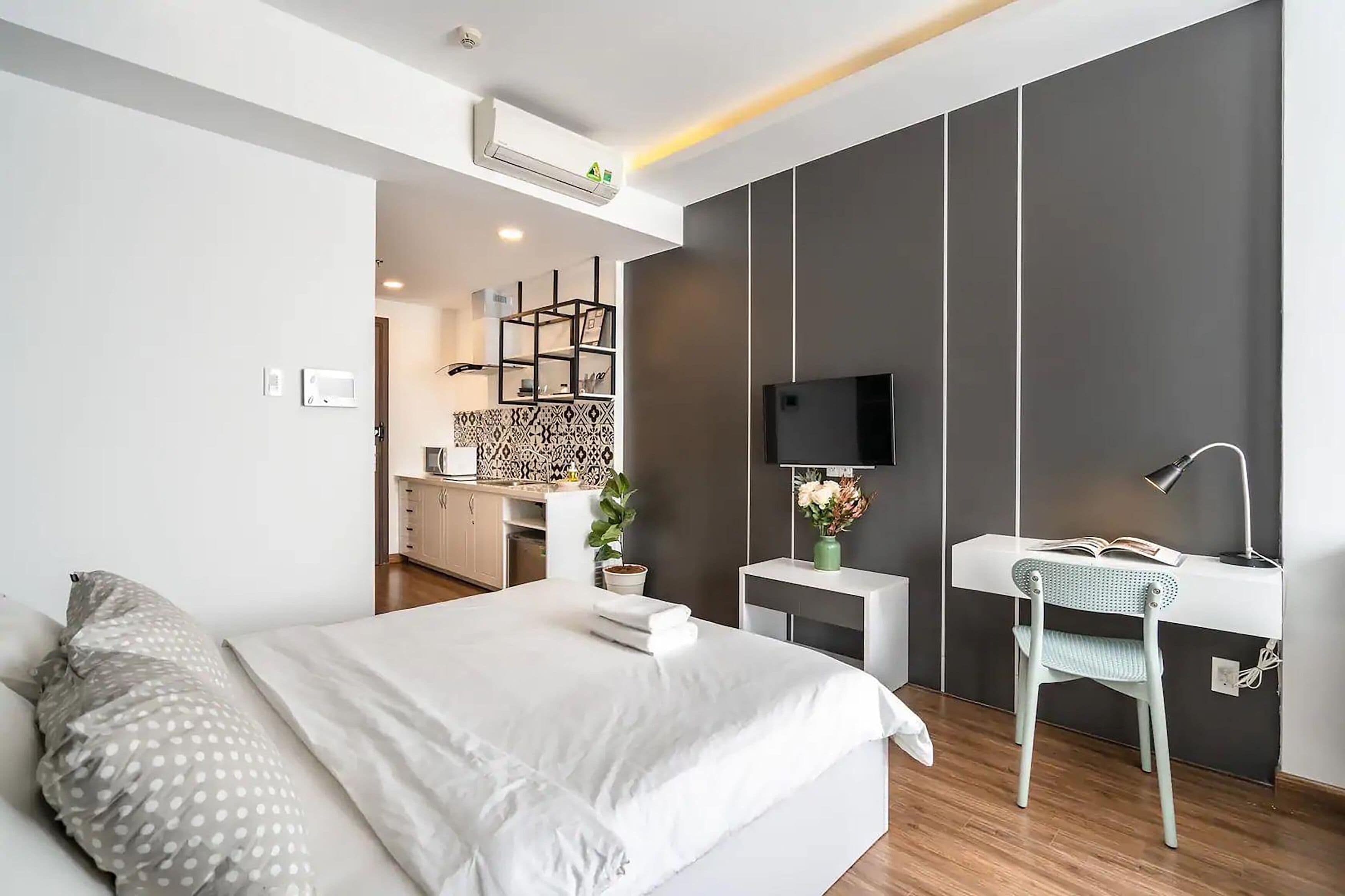 A modern hotel room with a bed, bedside table, chair, and a desk with a chair.
