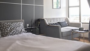 A modern hotel room with a large bed, a grey sofa, a small table, and a large window with curtains. - Saigon Sirius (Ho Chi Minh City)