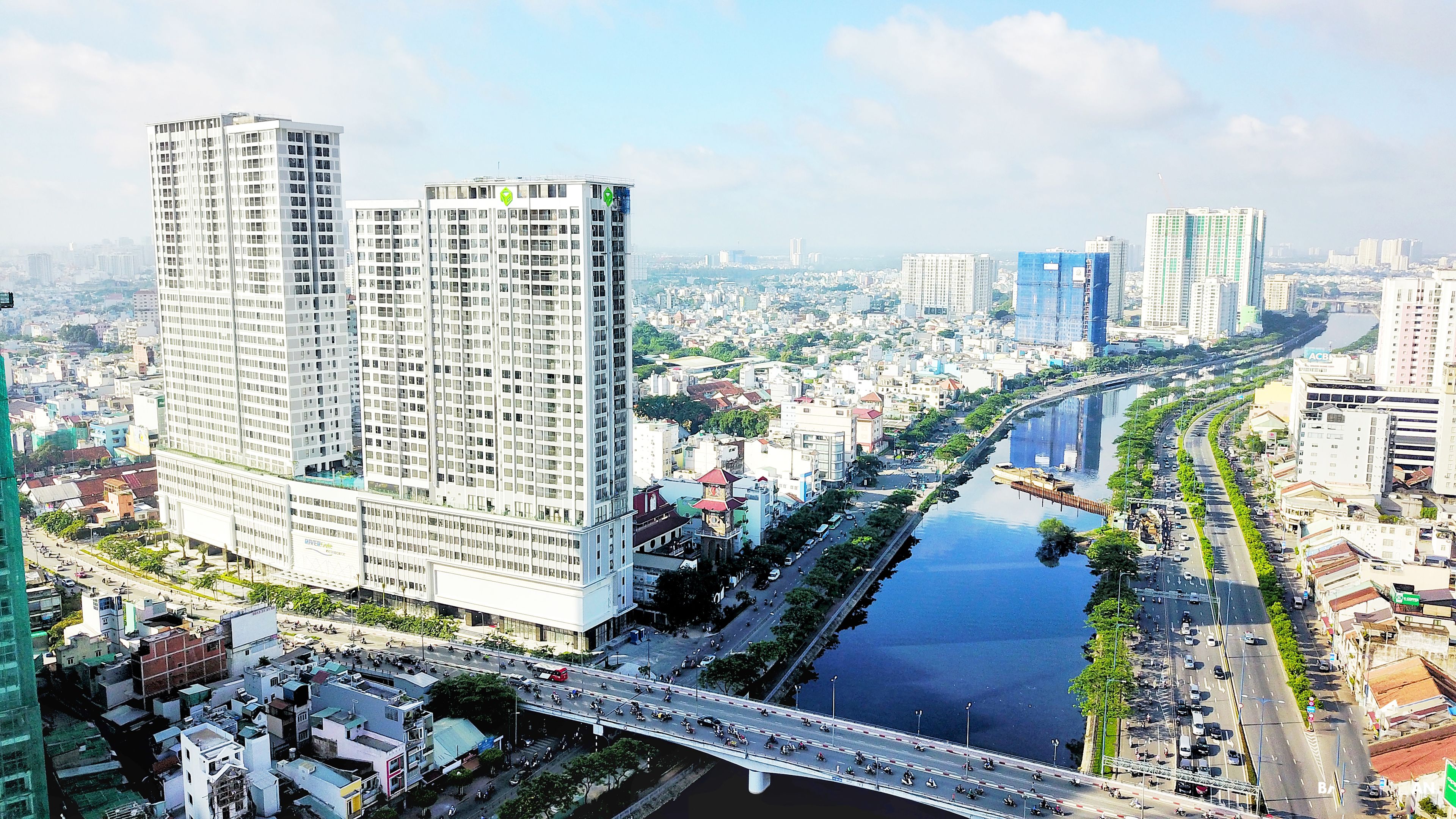 Un immeuble de grande hauteur à l’architecture moderne, entouré d’un environnement urbain dense, avec une rivière et un pont.