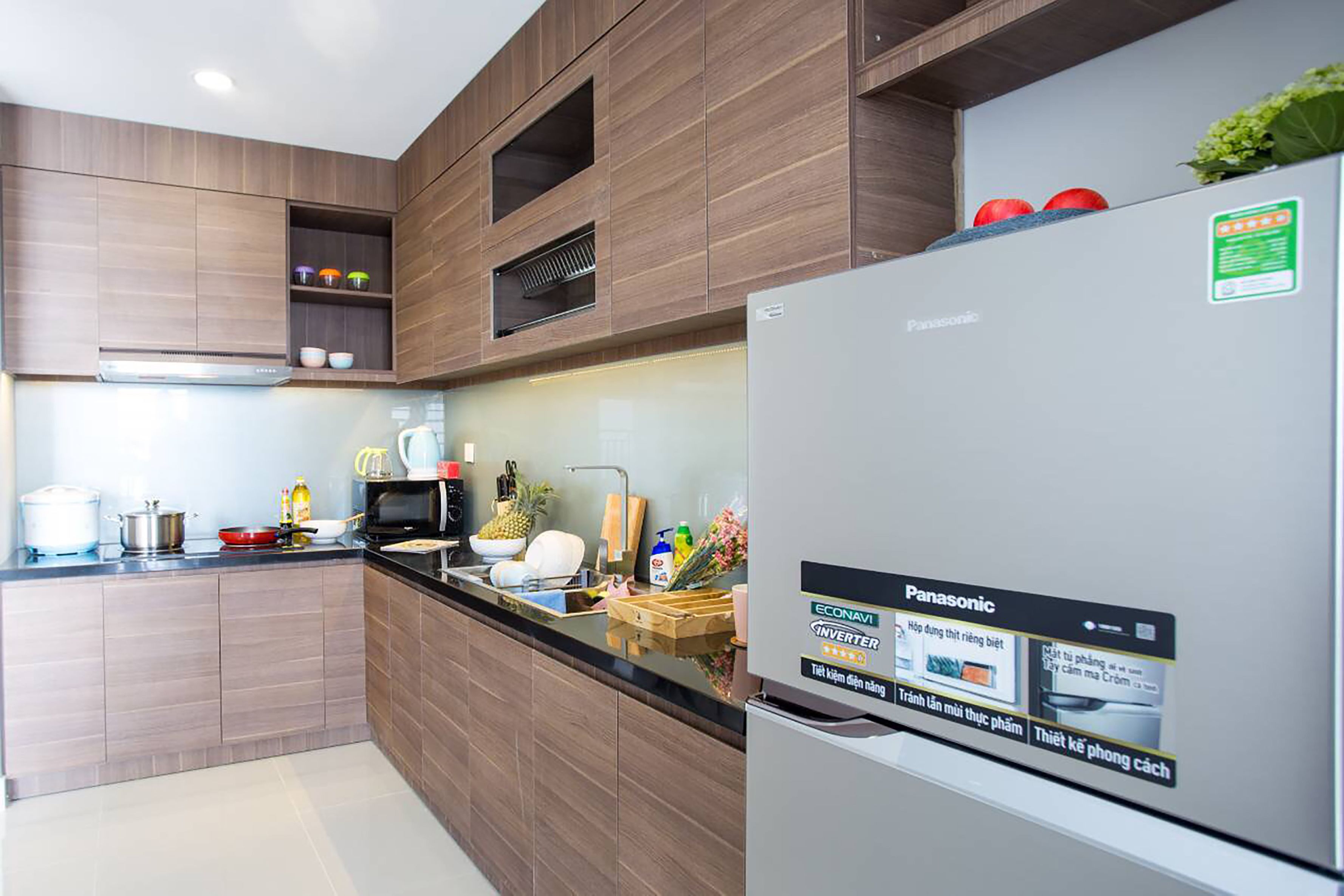 A modern kitchen with wooden cabinets, a stainless steel refrigerator, and a black countertop.