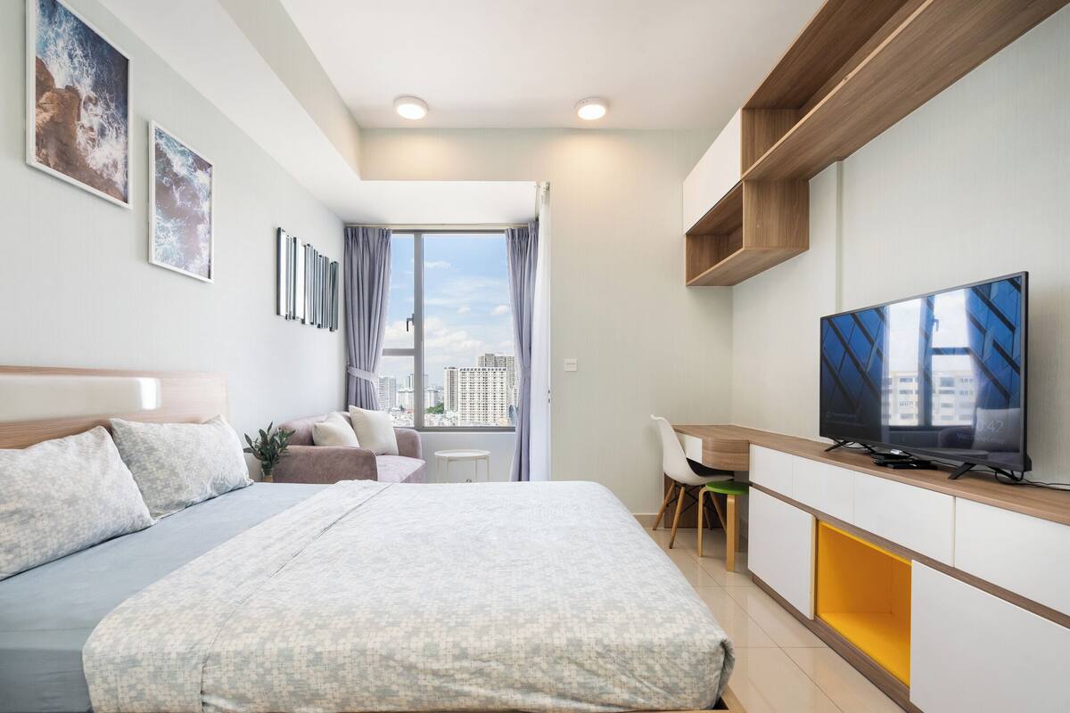 A modern hotel room with a bed, a desk, a television, and a city view.