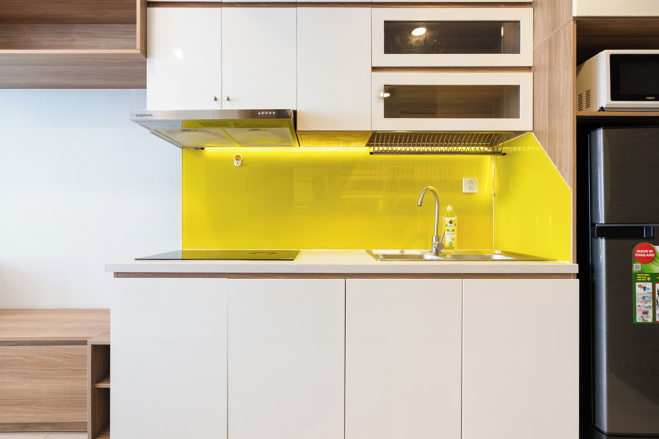 Una cocina con armarios blancos, salpicadero amarillo, pileta de acero inoxidable y refrigerador negro.