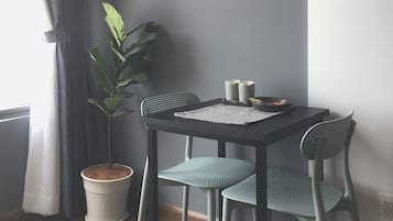 A small dining area with a table and two chairs, a potted plant, and a window with curtains.