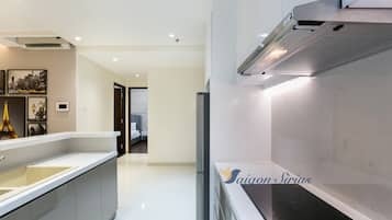 A modern kitchen with a built-in stove, a refrigerator, and a sink. There are framed pictures on the wall and a view into the adjacent bedroom.