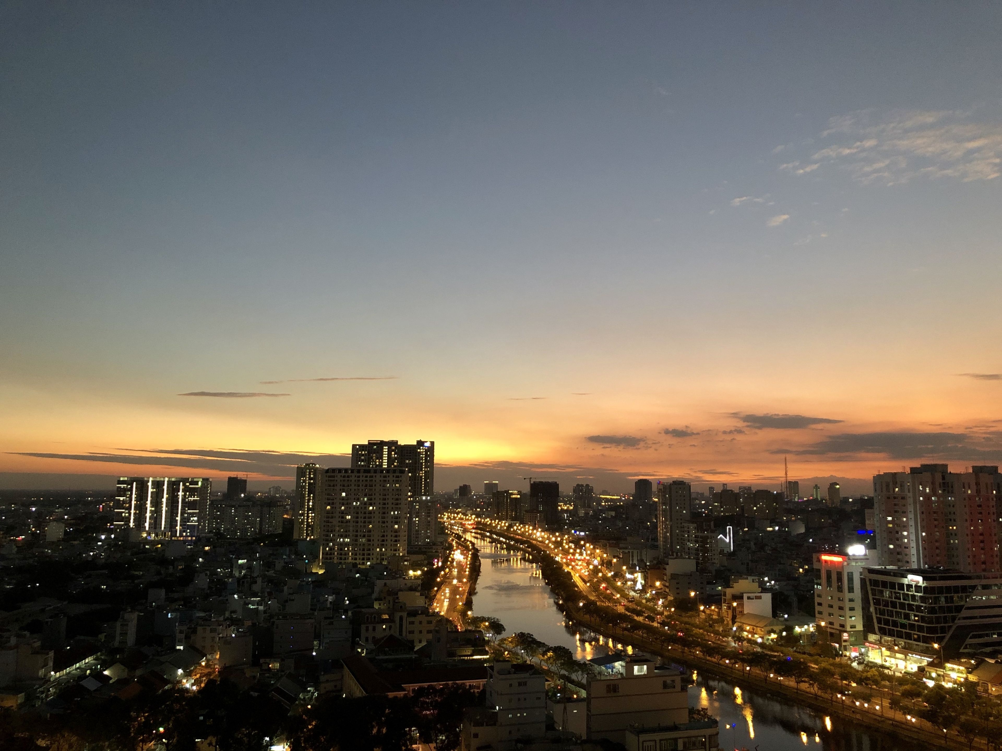 Un paisaje urbano al atardecer con un río serpenteando, edificios iluminados y una carretera con tráfico.