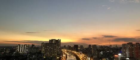 Un paisaje urbano al atardecer con un río serpenteando, edificios iluminados y una carretera con tráfico.