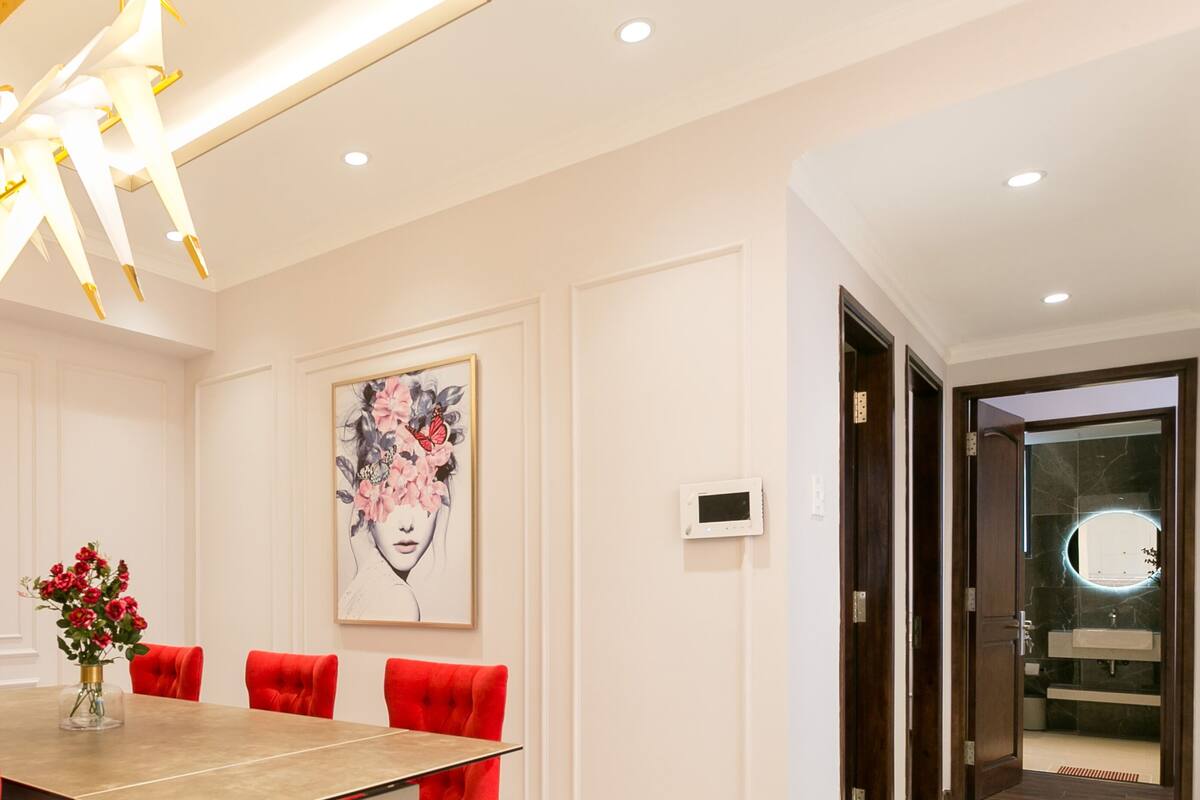 A modern dining room with a long table, red chairs, a chandelier, and a framed artwork on the wall.