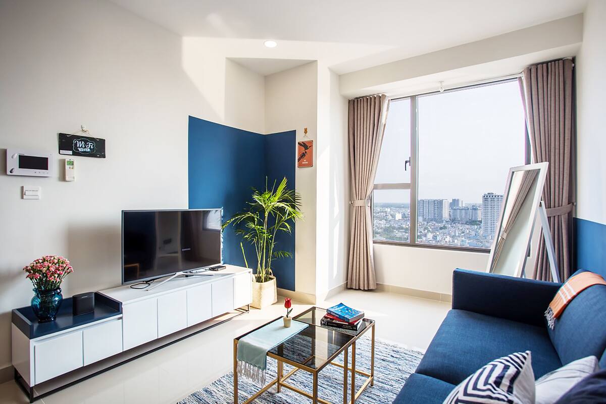 A modern living room with a TV, sofa, coffee table, and a large window with curtains.