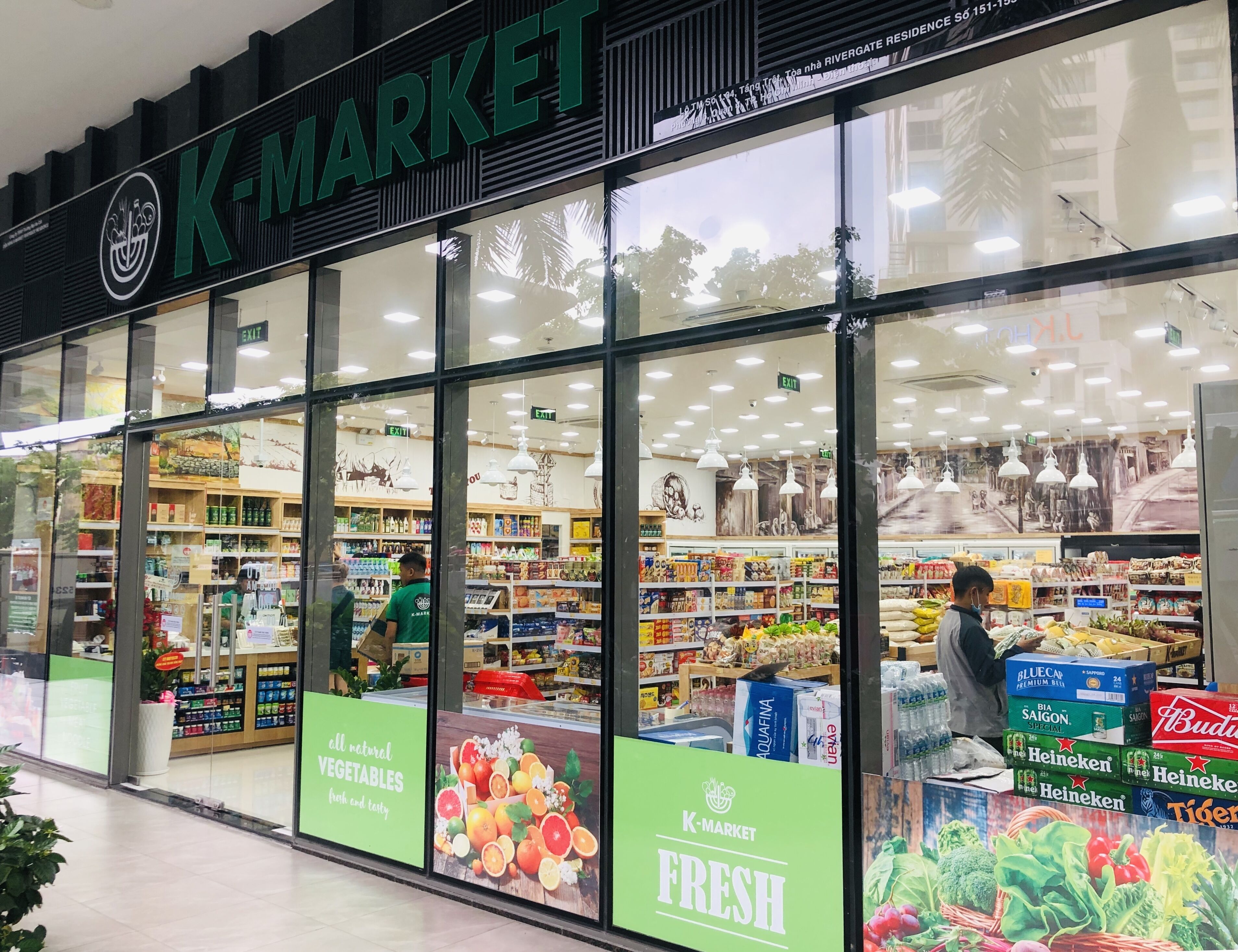 A K-Market store with large glass windows, shelves stocked with various products, and signs advertising fresh produce.