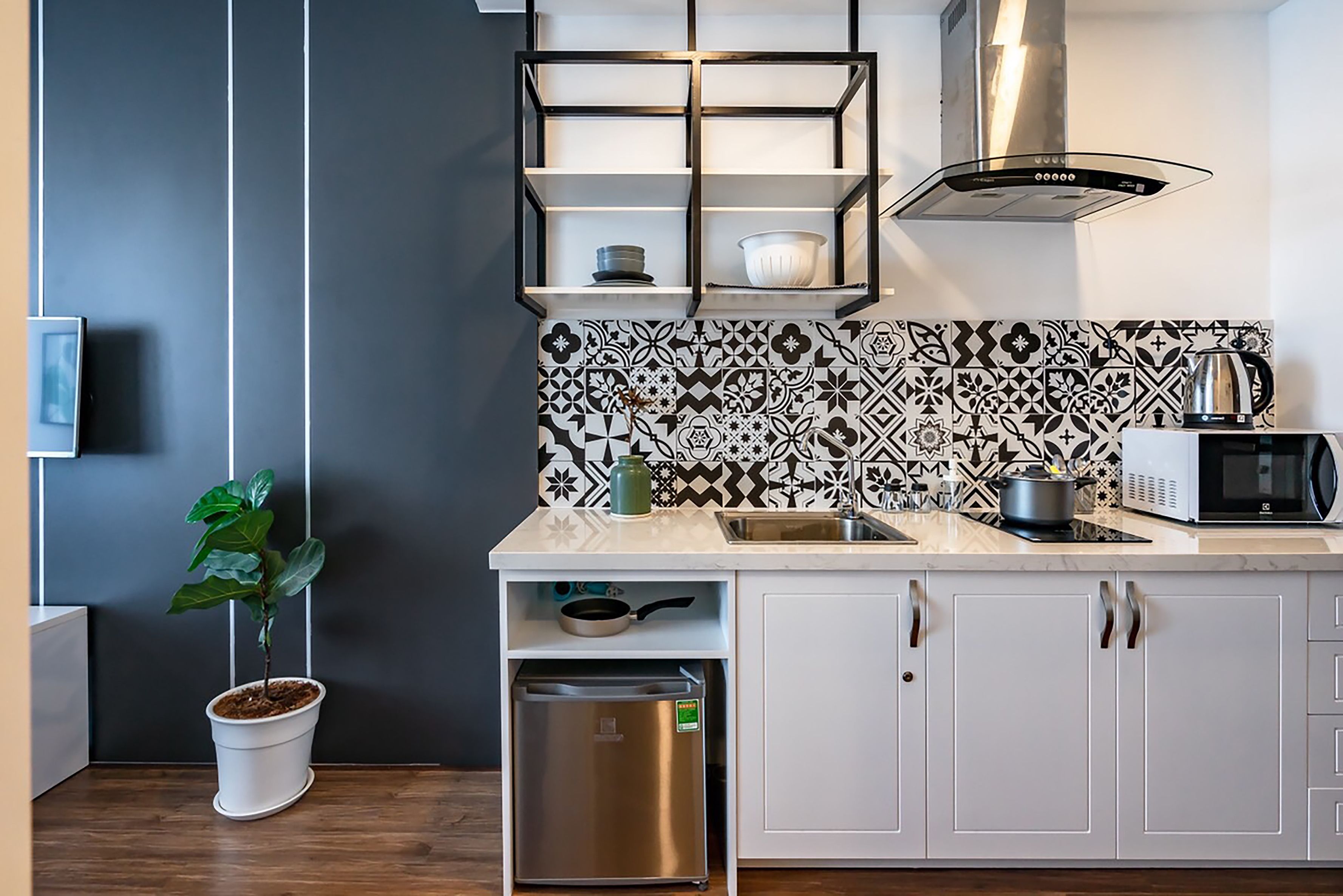 A modern kitchen with white cabinets, a stainless steel refrigerator, a microwave, and a patterned backsplash.