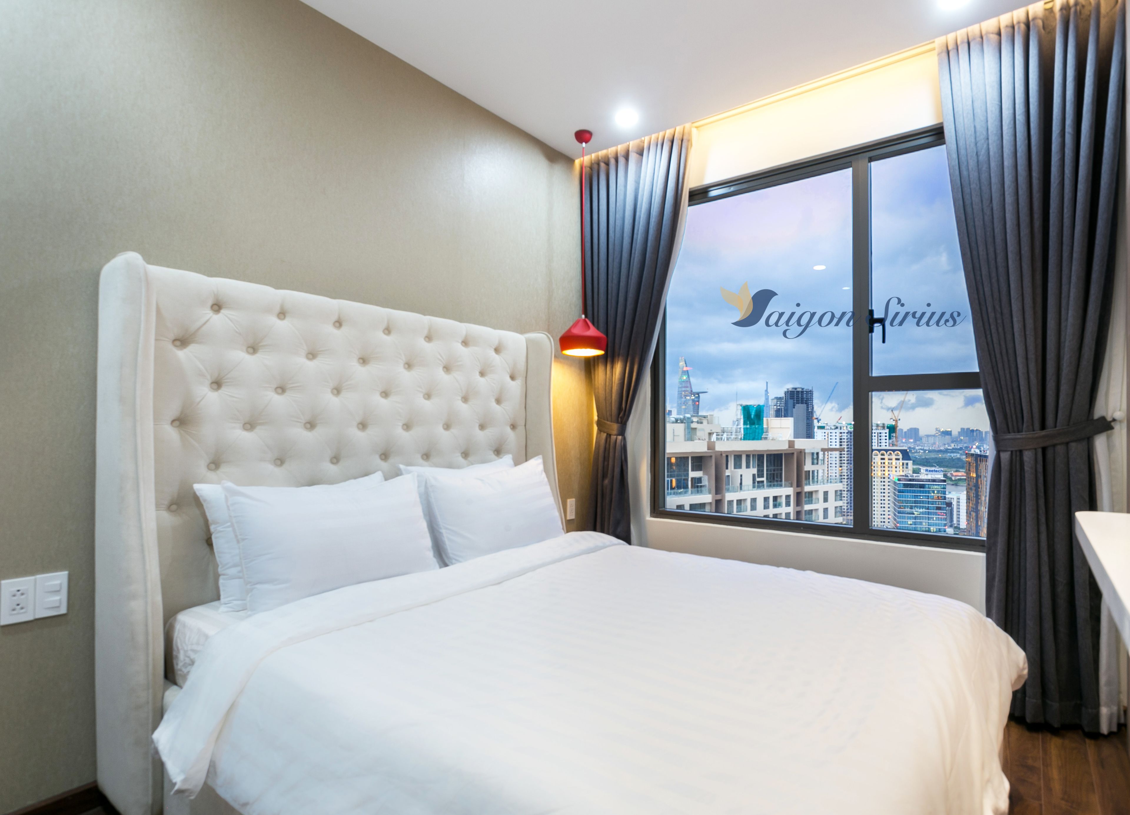 Habitación de hotel con una cama grande, vistas de la ciudad a través de una ventana y una lámpara roja en la mesita de noche.