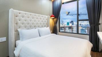Habitación de hotel con una cama grande, vistas de la ciudad a través de una ventana y una lámpara roja en la mesita de noche.