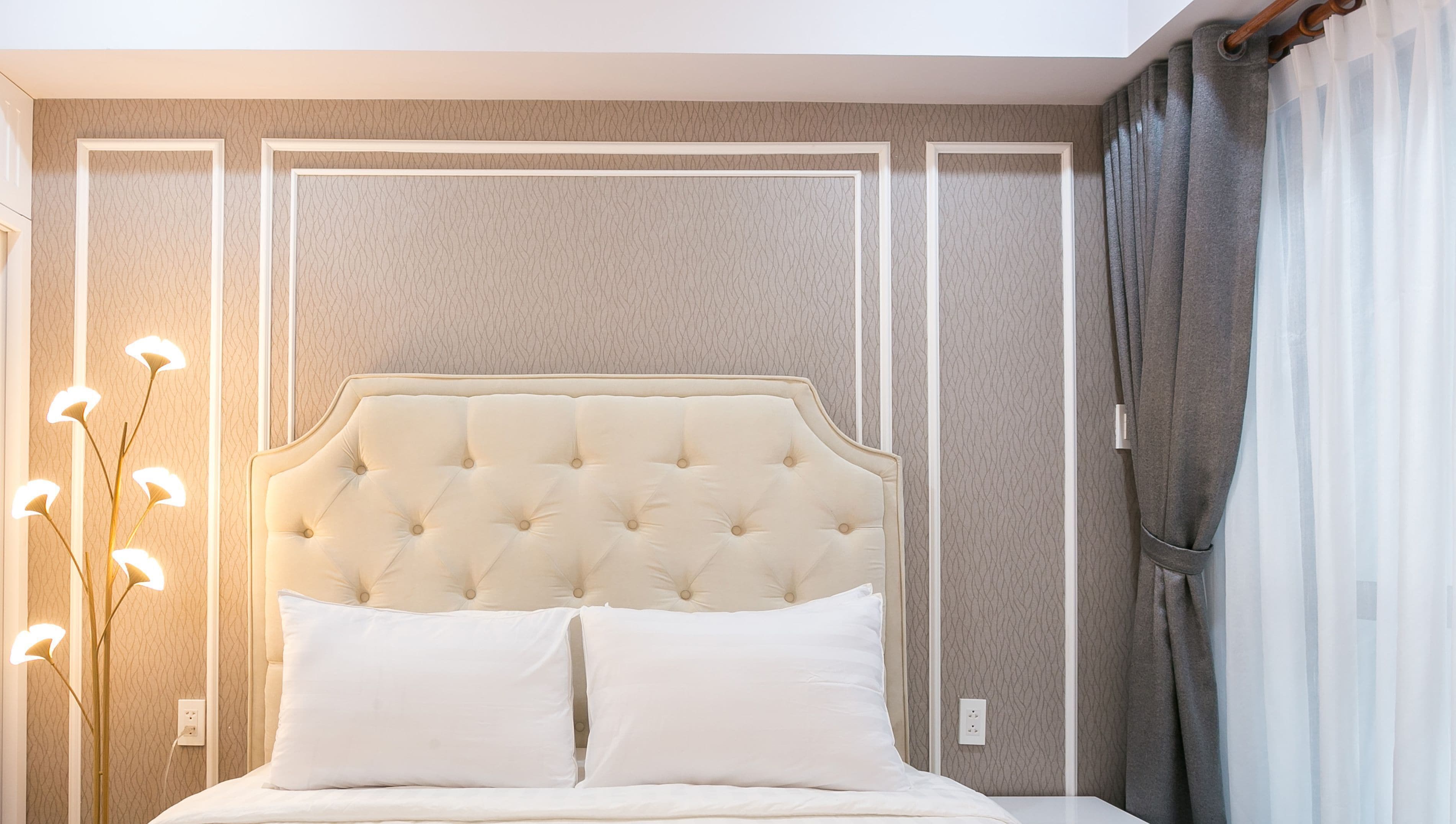 Un dormitorio ordenado con un cabecero capitonado, dos almohadas blancas y una lámpara de noche.