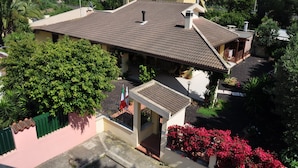 Ein Haus mit Ziegeldach, einer kleinen Veranda und einem Garten mit roten Blüten.