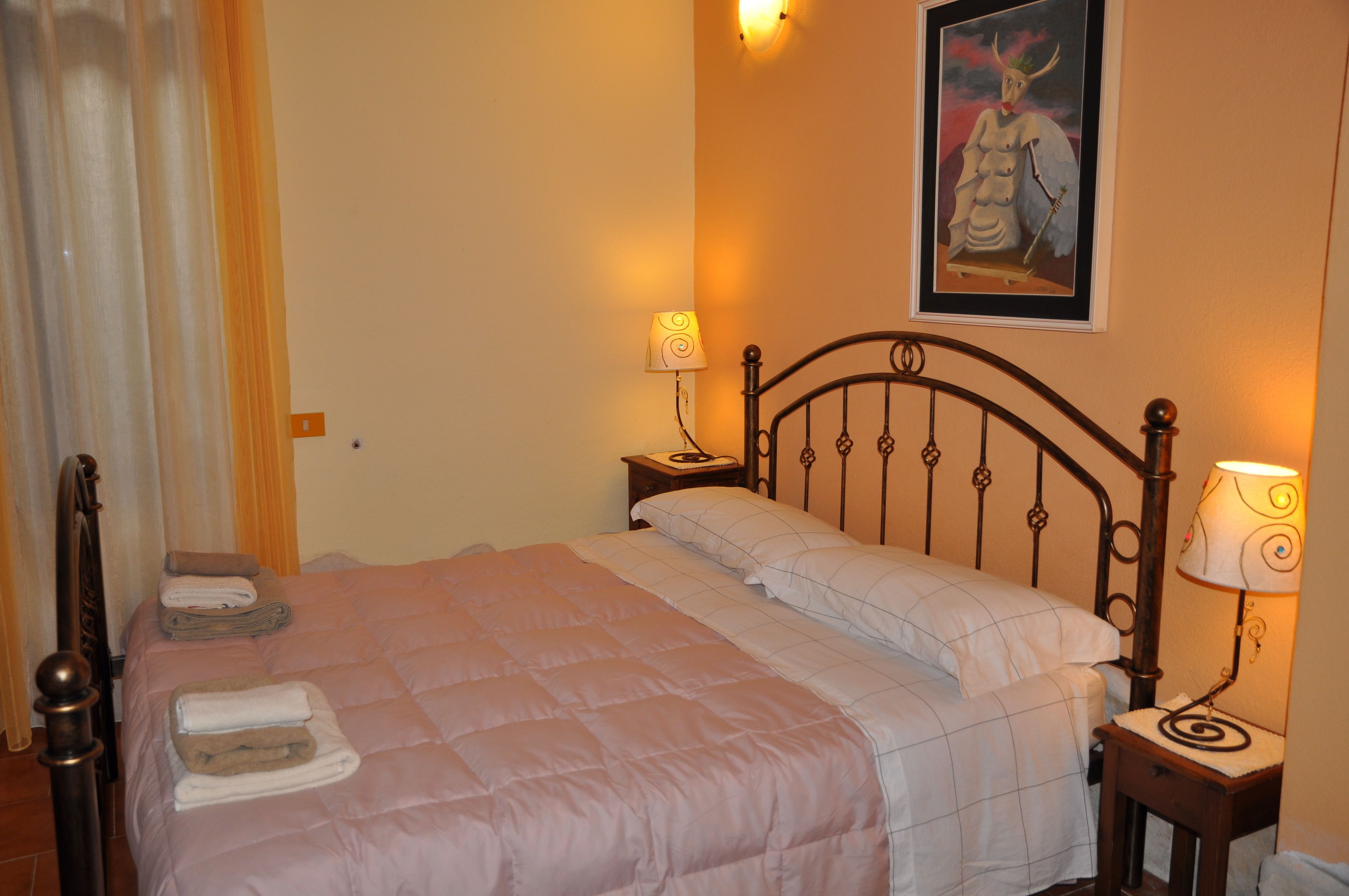 Cama bem arrumada com colcha rosa, duas mesas de cabeceira com abajures e um quadro na parede.