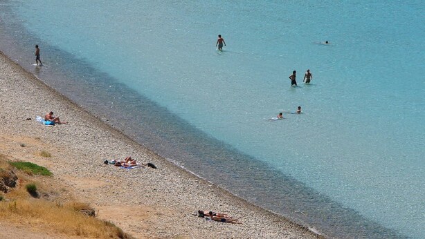 Ein Strand mit klarem Wasser, Menschen beim Schwimmen und Sonnenbaden.