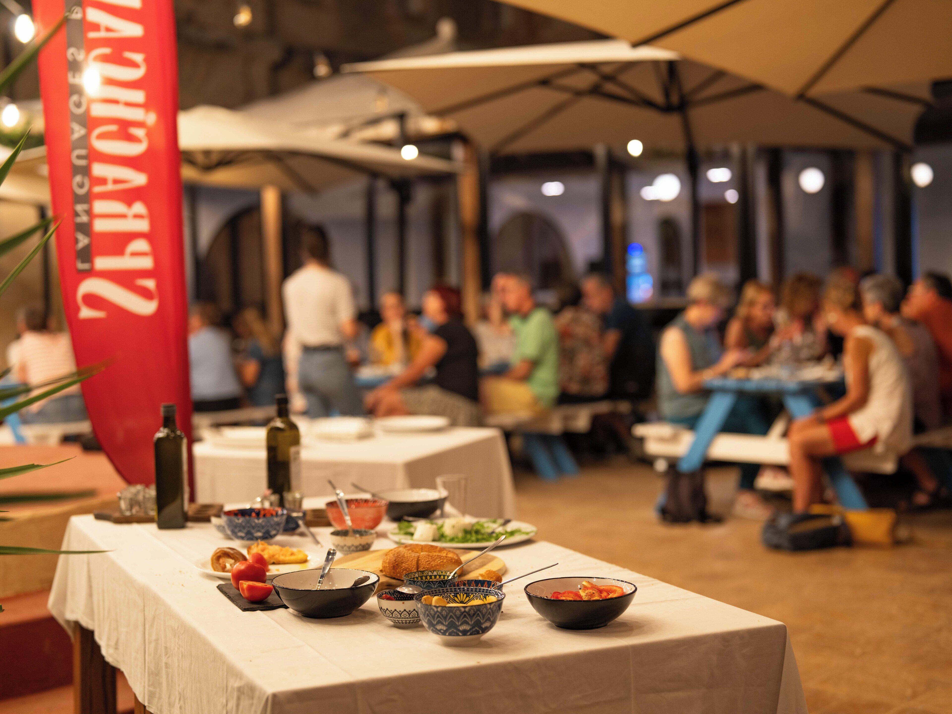 A dining area with tables set for a meal, a red flag with text, and people seated at tables.