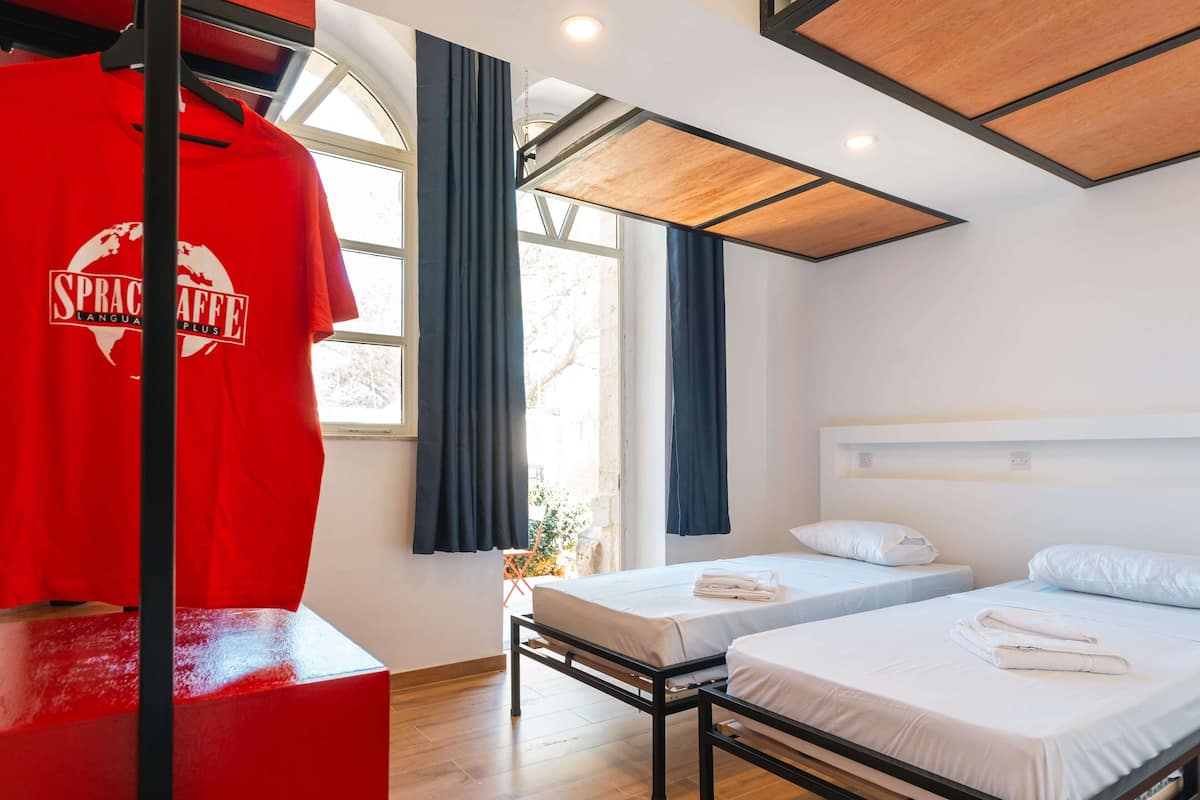 Habitación de hotel con dos camas, una camiseta roja en un perchero y una ventana con cortinas.