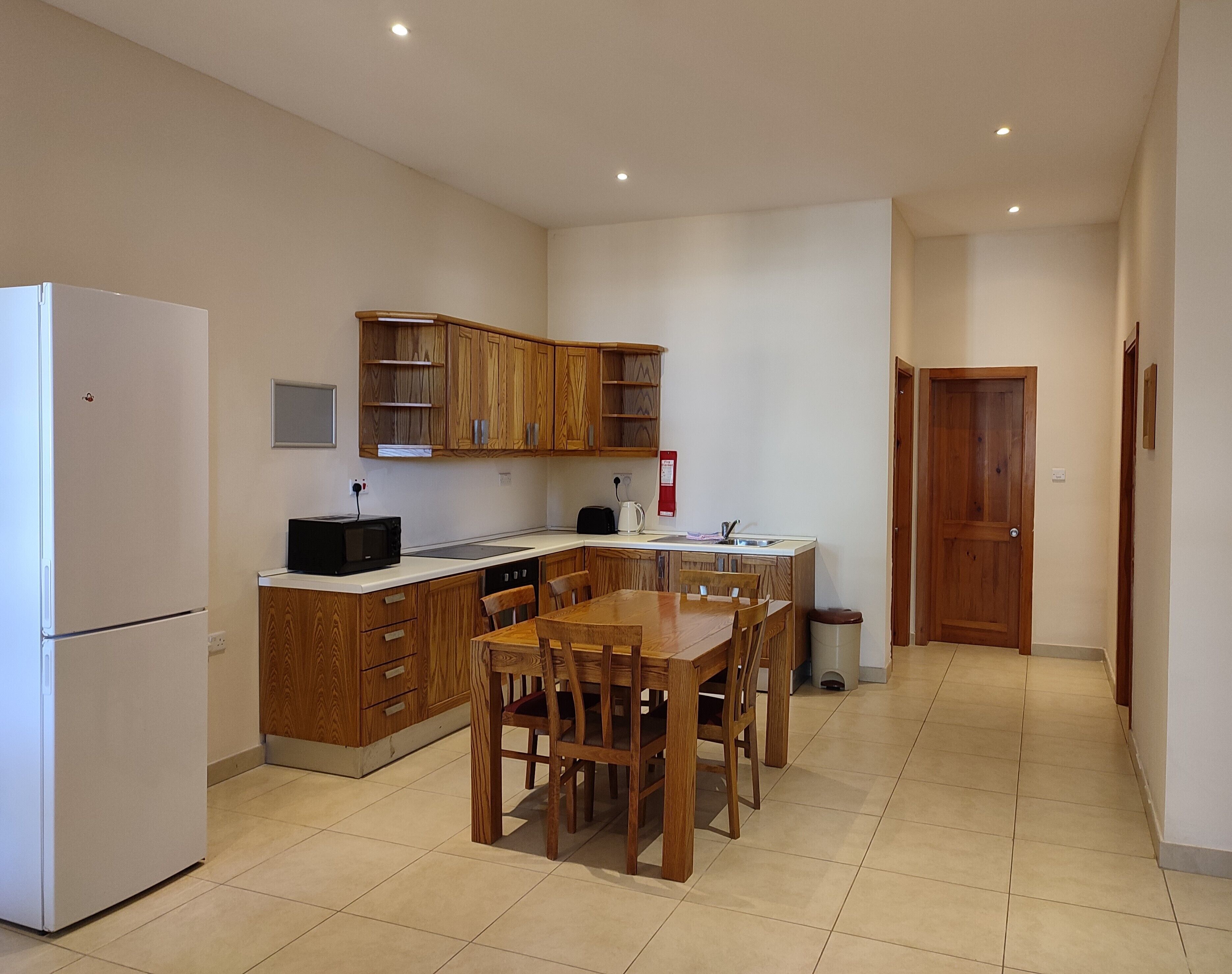 Une cuisine compacte avec des meubles en bois, un réfrigérateur blanc, une table à manger avec des chaises et un petit évier.