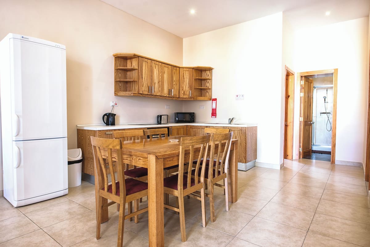 Una cocina compacta con armarios de madera, un refrigerador blanco, un microondas y una mesa de comedor con sillas.