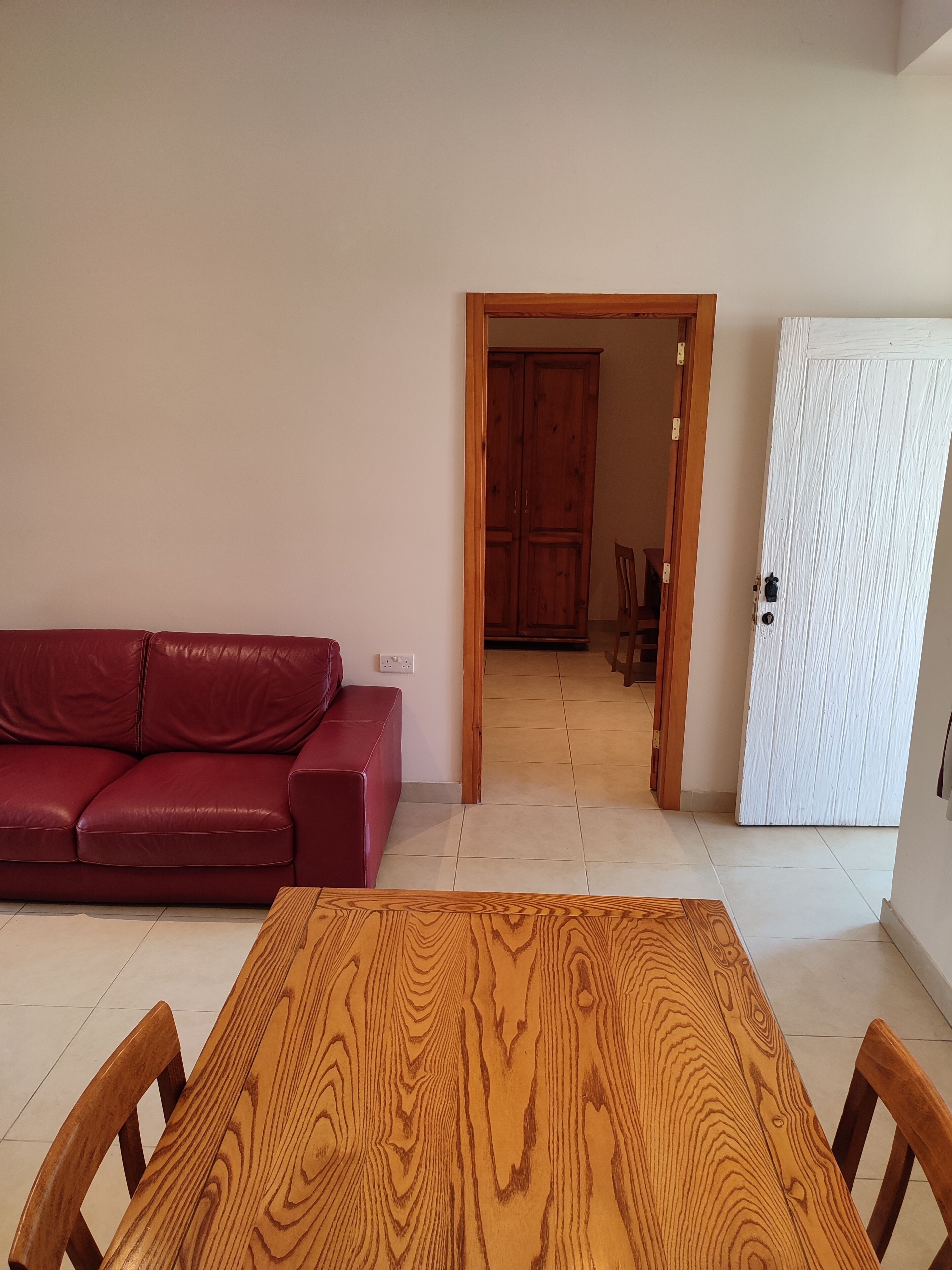 A room with a wooden dining table, a red leather sofa, and a white door.