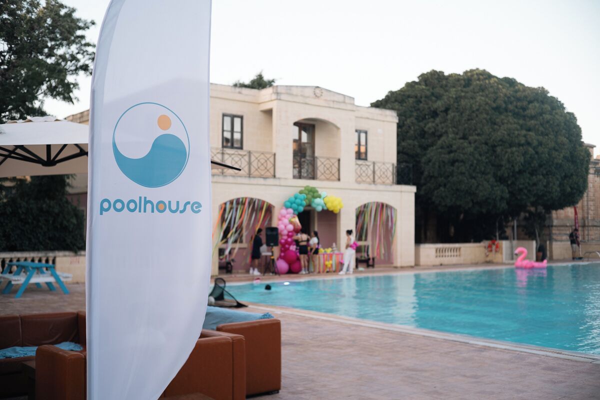 A pool area with a lounge chair, a pool, and a building with a balcony.