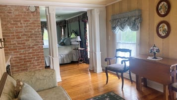 Una habitación con piso de madera, un tapete floral verde, un escritorio de madera, una silla, una cama con cabecera verde y una pared de ladrillo.