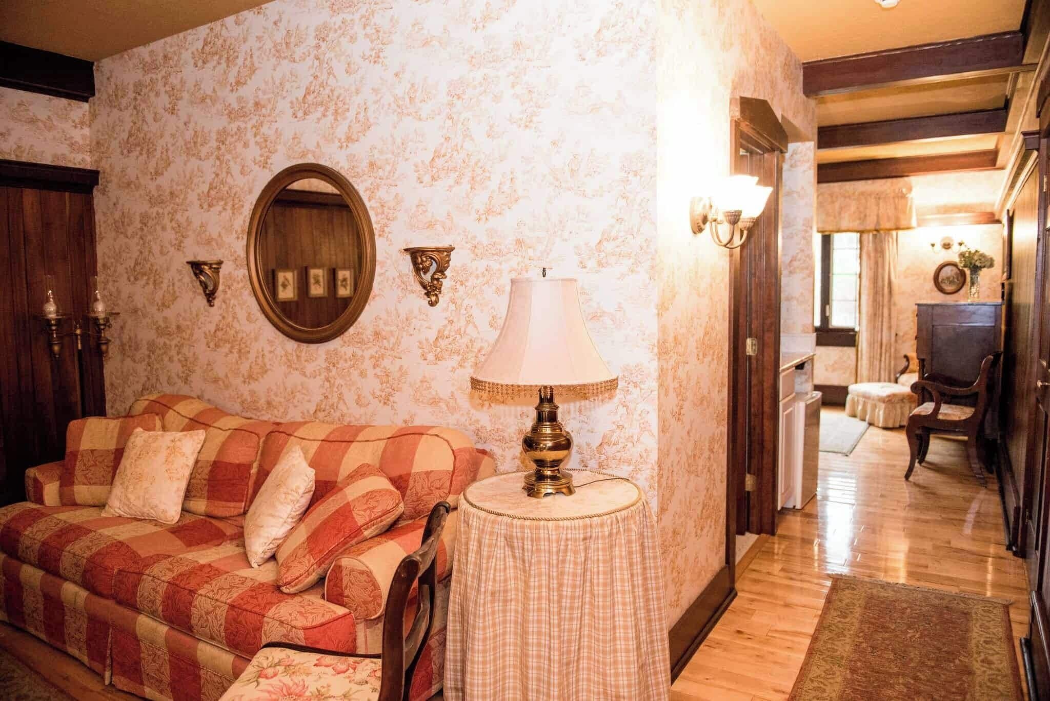A cozy living room with a checkered sofa, a round table with a lamp, and a mirror on the wall.
