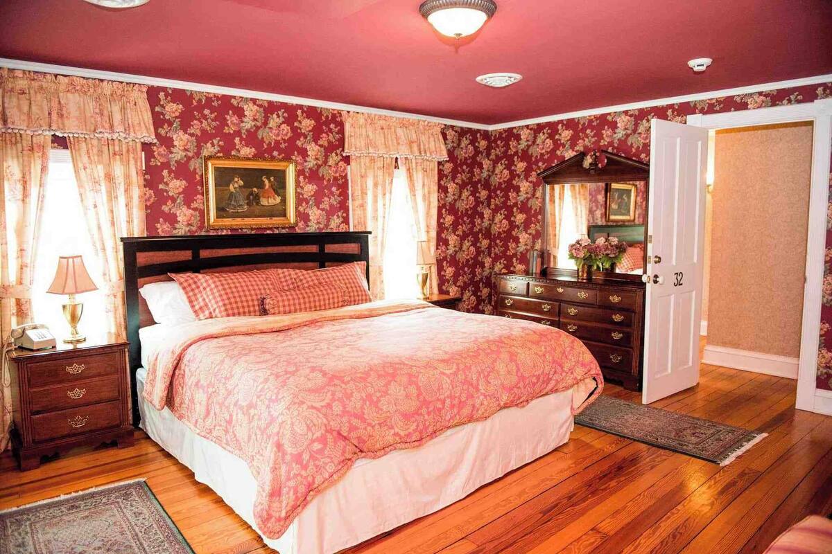 A bedroom with a large bed, wooden dresser, and a door leading to another room.
